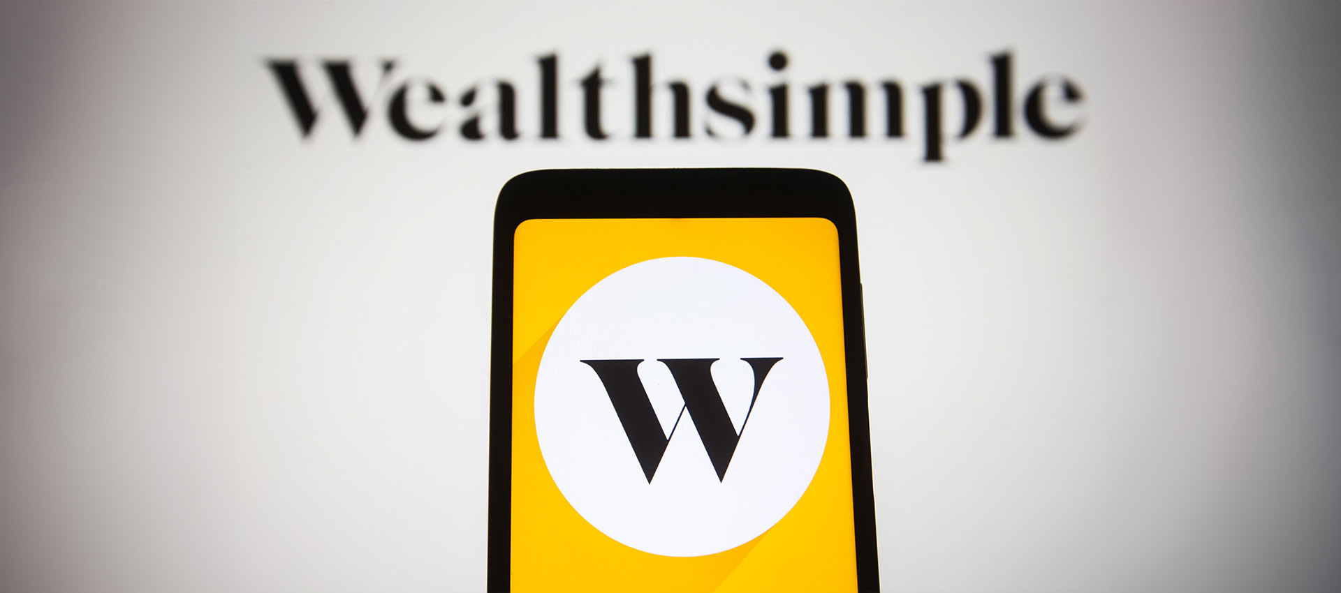 Wealthsimple black "W" on white circle with yellow background displayed on mobile device with "Wealthsimple" word mark on grey background 